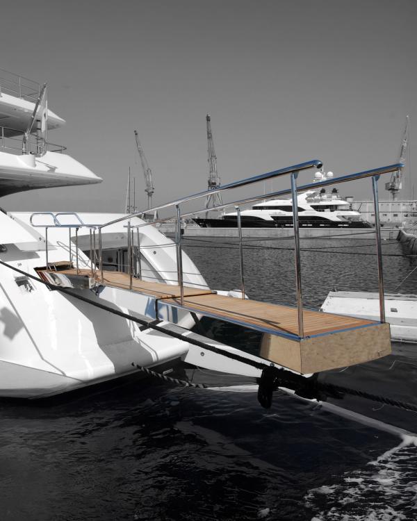 Passerella per yachts in acciaio inox con piano in teak, installata a poppa di un’imbarcazione di lusso in porto.